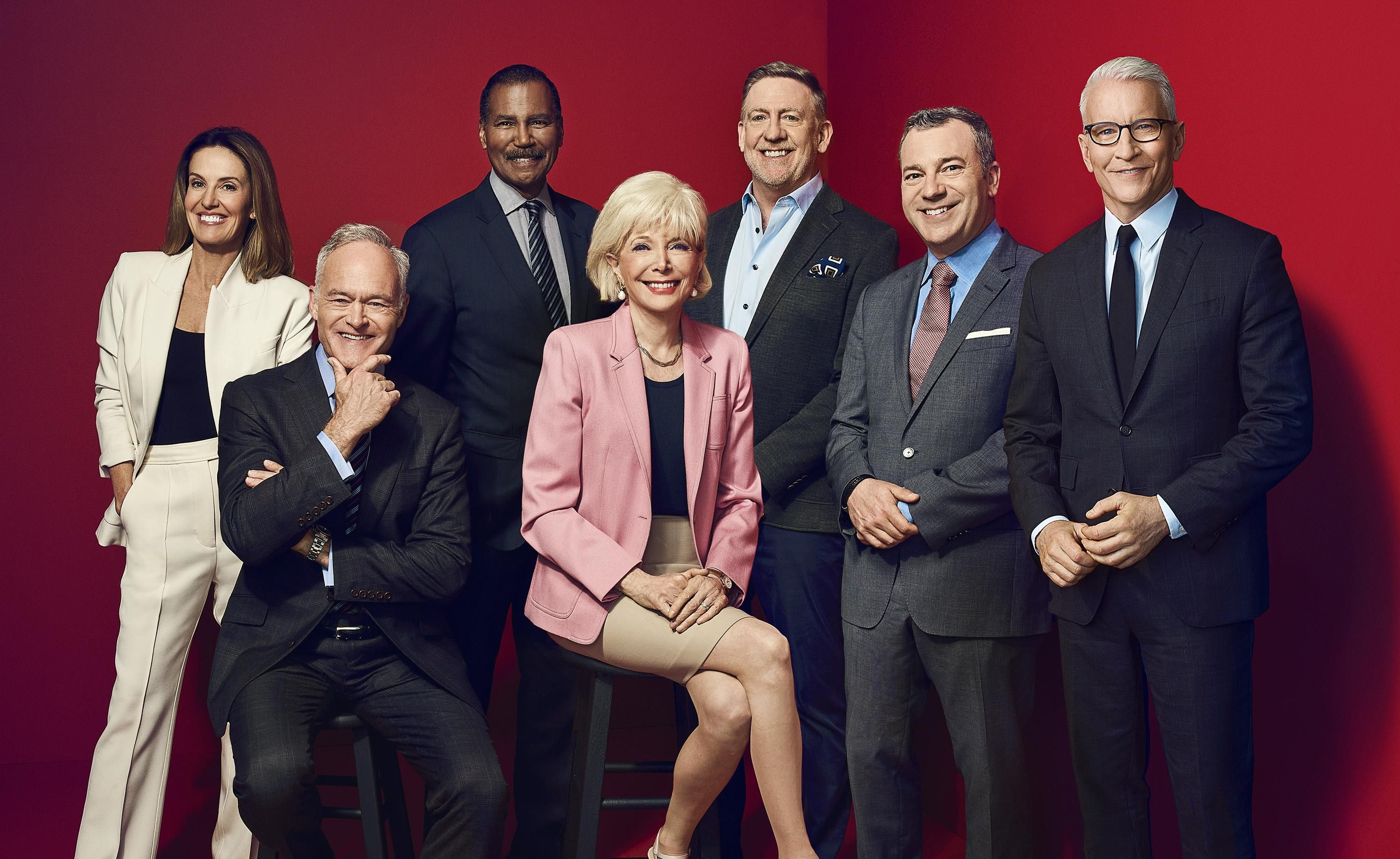 The 60 Minutes crew poses smiling against a red backdrop.