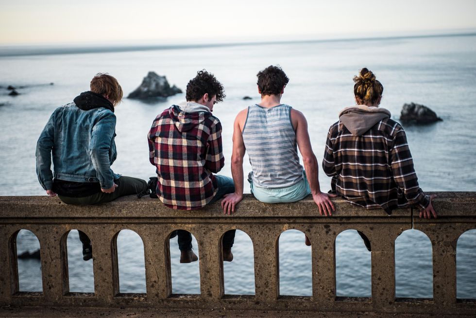 Four young people sitting on bridge over of body of water.