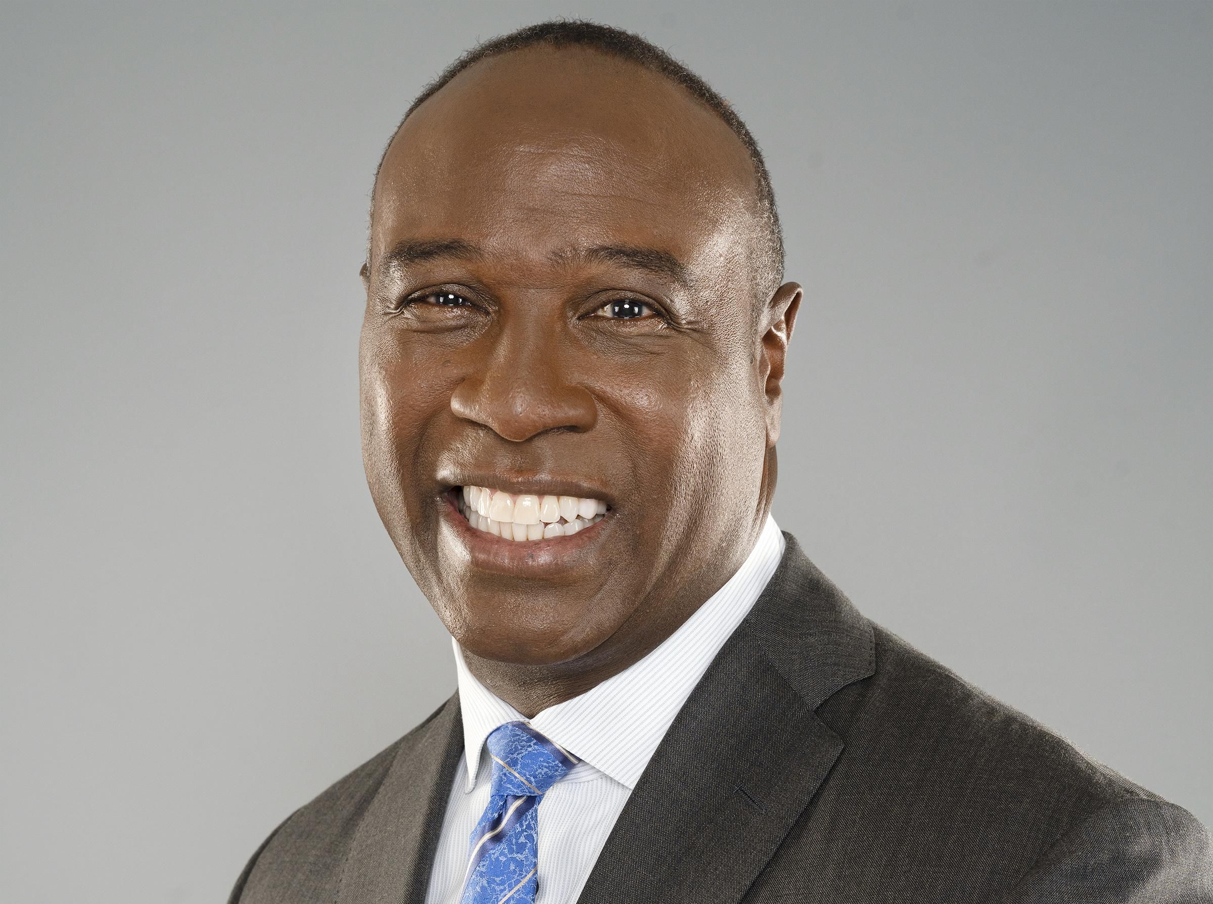 Charles Davis of the NFL on CBS smiles while wearing grey suit and light blue tie.