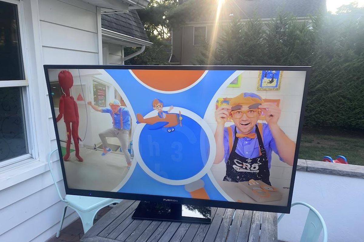 a photo of Furrion Aurora Full Sun Smart 4K UHD LED Outdoor TV on a table in a backyard.