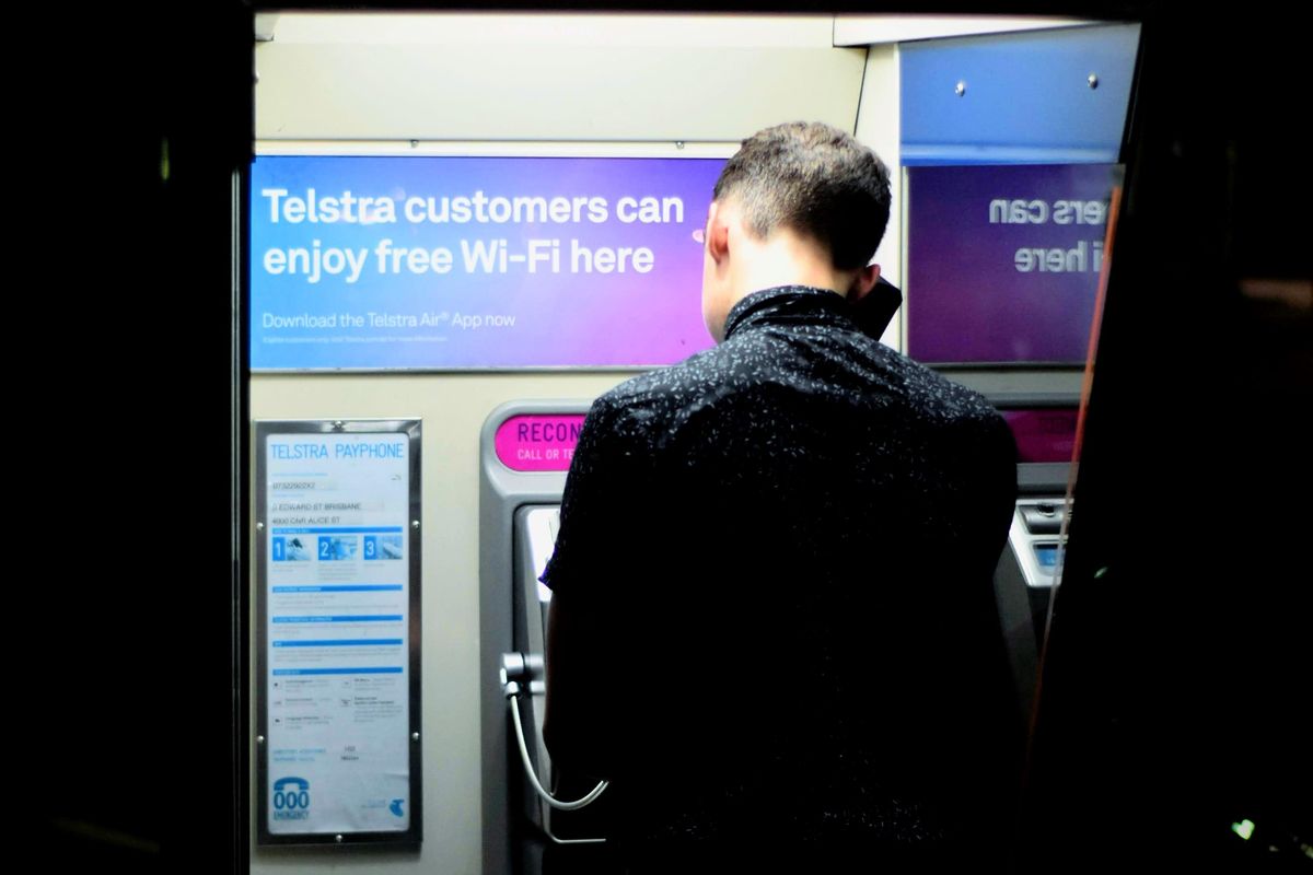 men in black coat using a pay phone