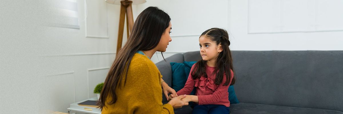 a mother talking to her little daughter while the daughter sits in a sofa