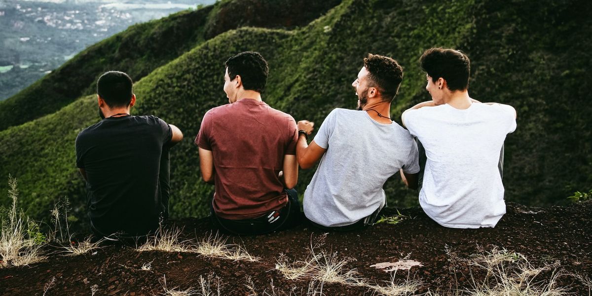 Four young men sit on a mountainside while laughing and talking
