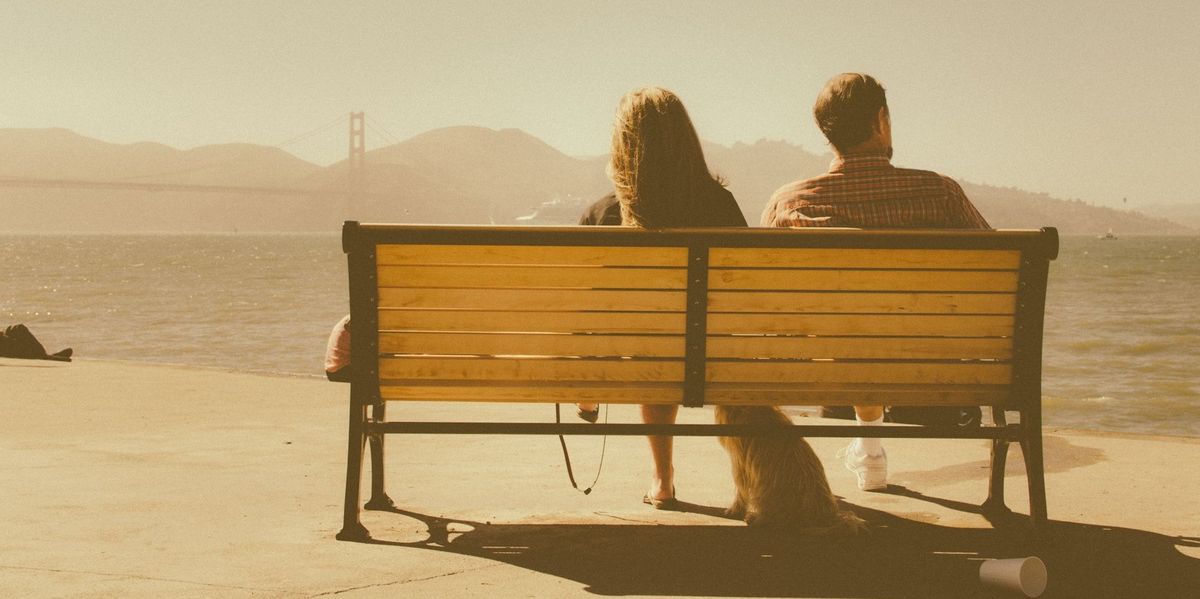 A couple with their backs to the camera sits on a bench looking out thinking