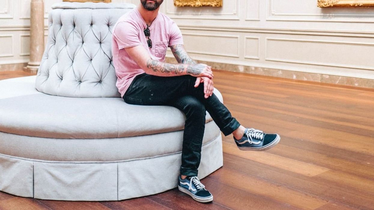 Man wearing pink shirt and sitting with legs crossed inside an art gallery.