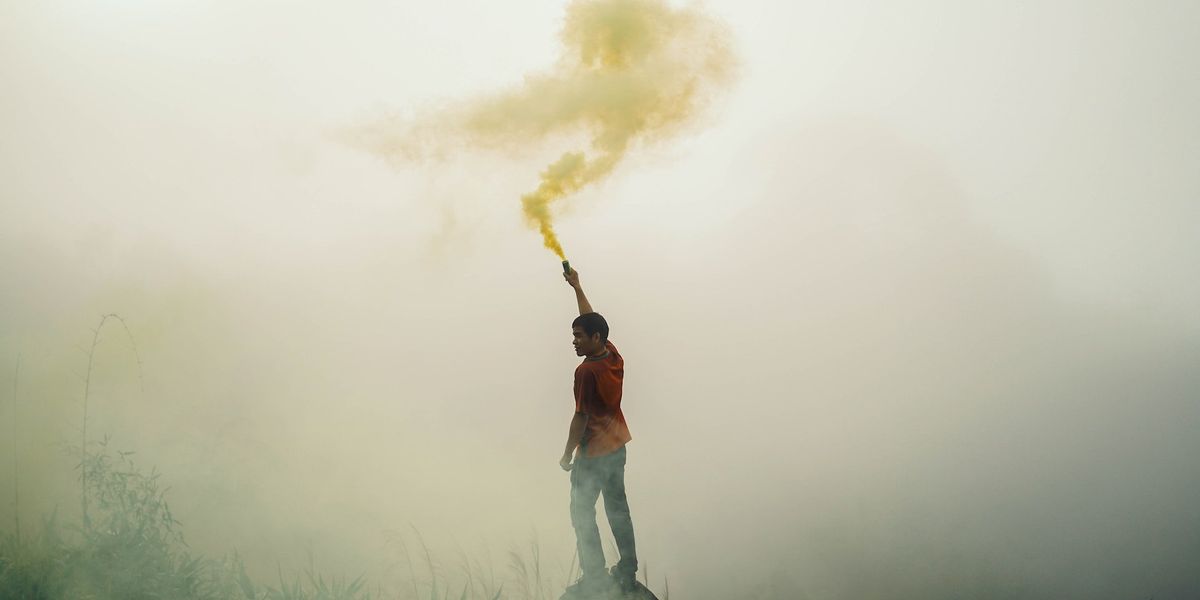 A young man stands on a hill and waves a smoke signal