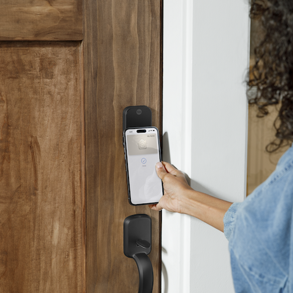 a photo of a woman using Apple Home Keys on her smartphone to control her Yale Assure Lock 2 Plus 