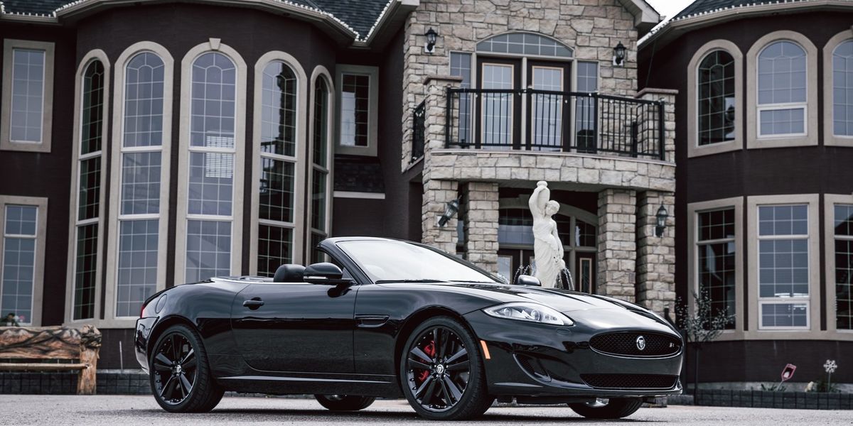 An expensive car sits in front of fabulous, expensive house with a statue