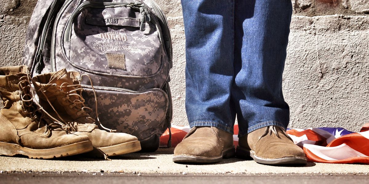 Legs of a Military recruit next to their personal belongings and American flag