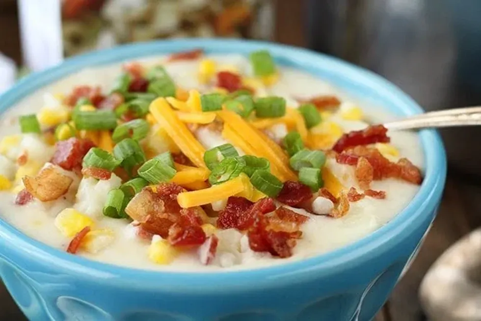 A blue bowl of bacon corn chowder topped with bacon, chives and cheese.