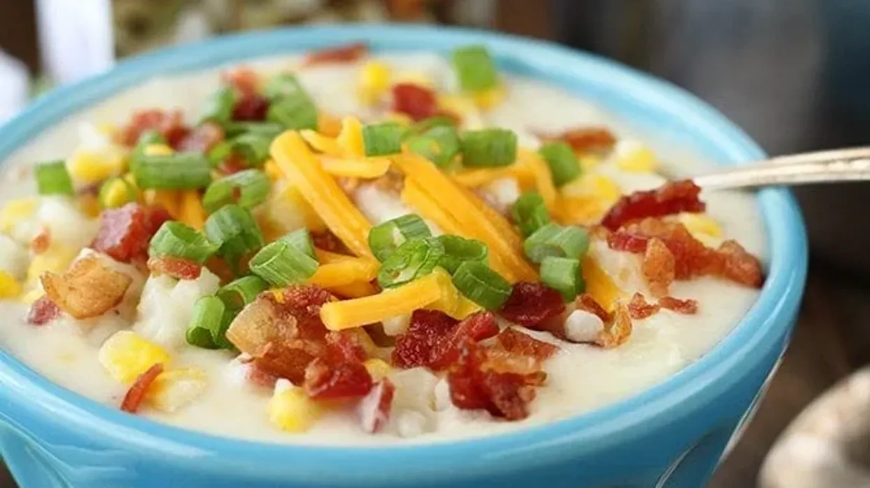 A blue bowl of bacon corn chowder topped with bacon, chives and cheese.