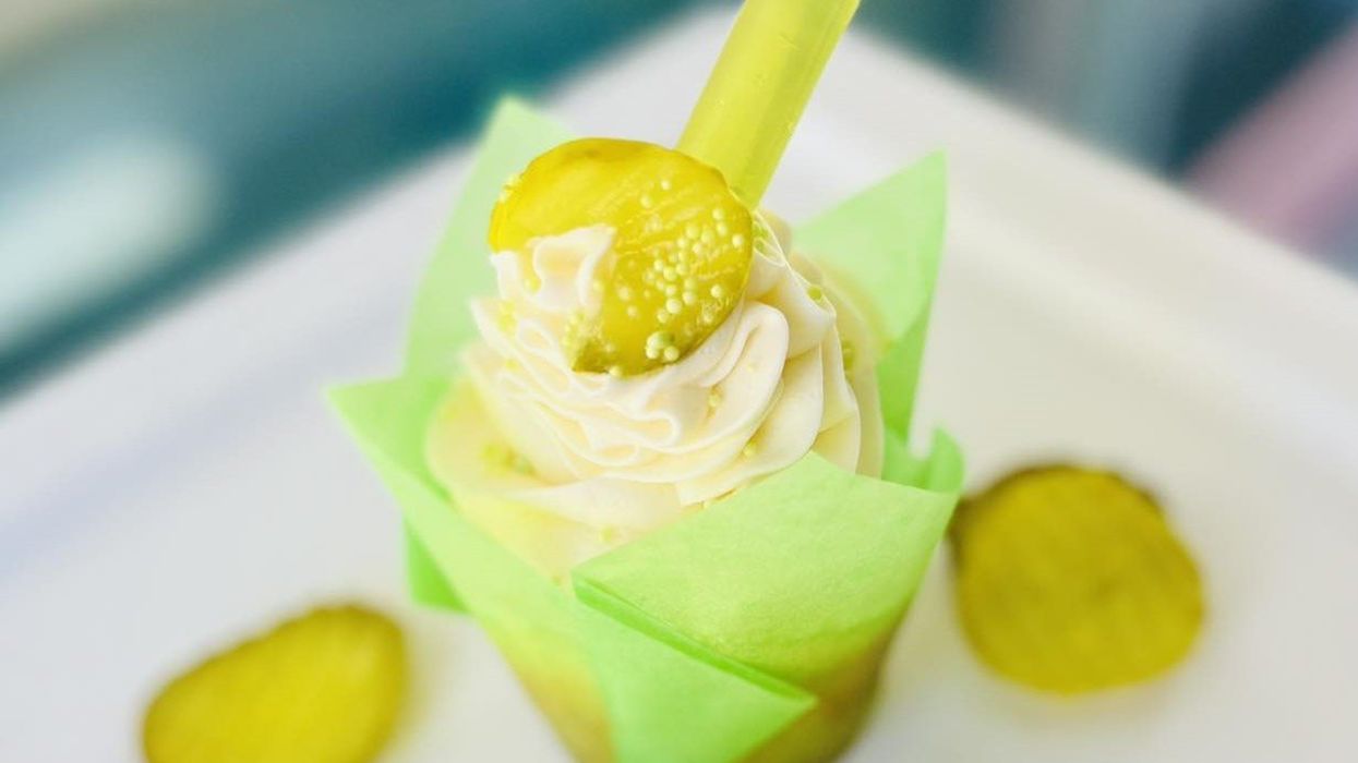 A dill pickle cupcake in a green wrapper on a plate surrounded by pickle chips.