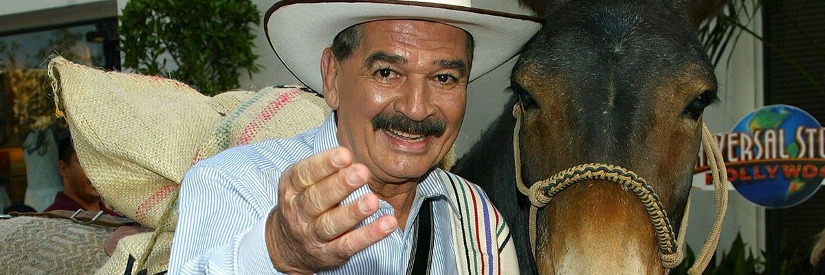 Colombian man wearing a white cowboy hat stands in front of a horse 