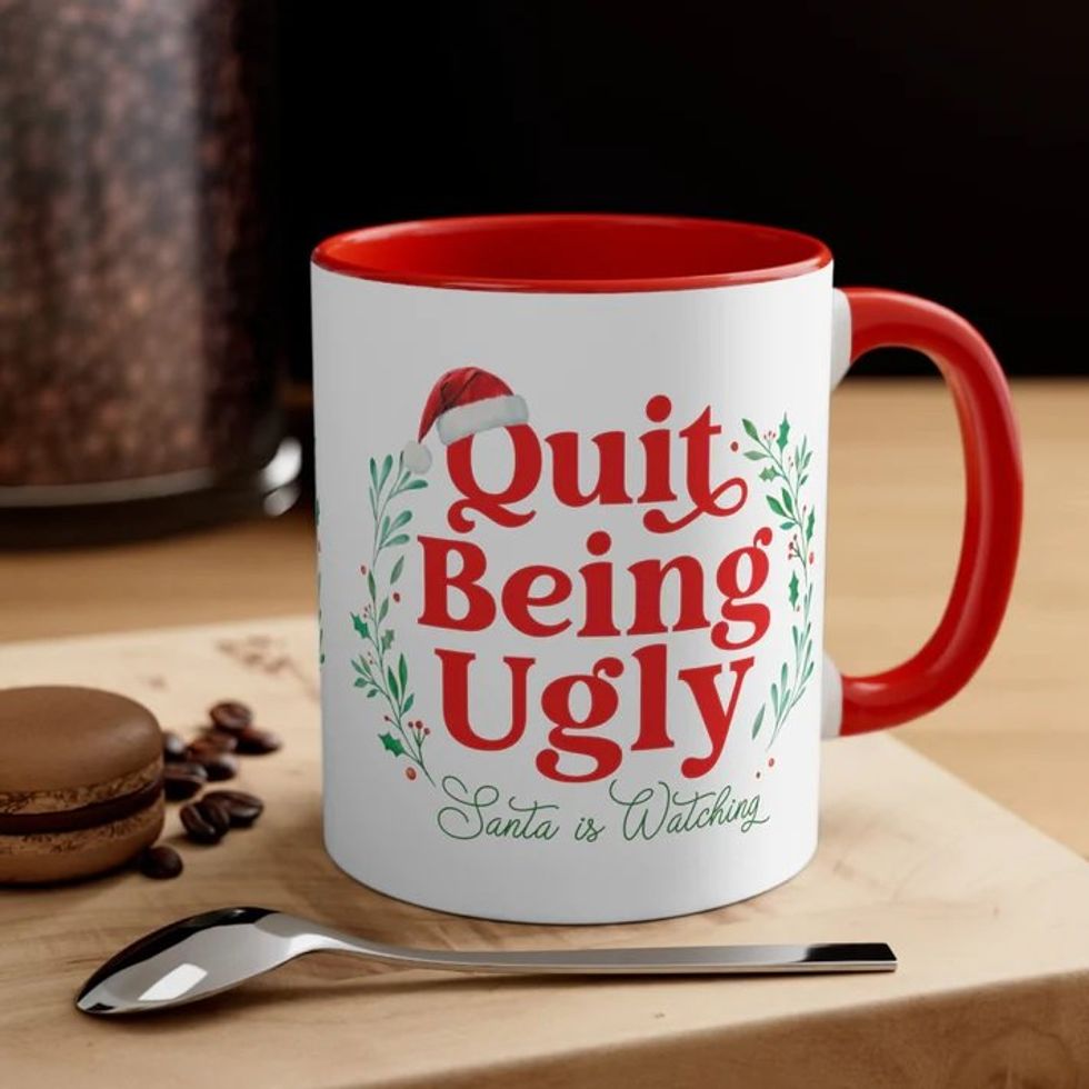 A white coffee cup that says "Quit Being Ugly: Santa is Watching."