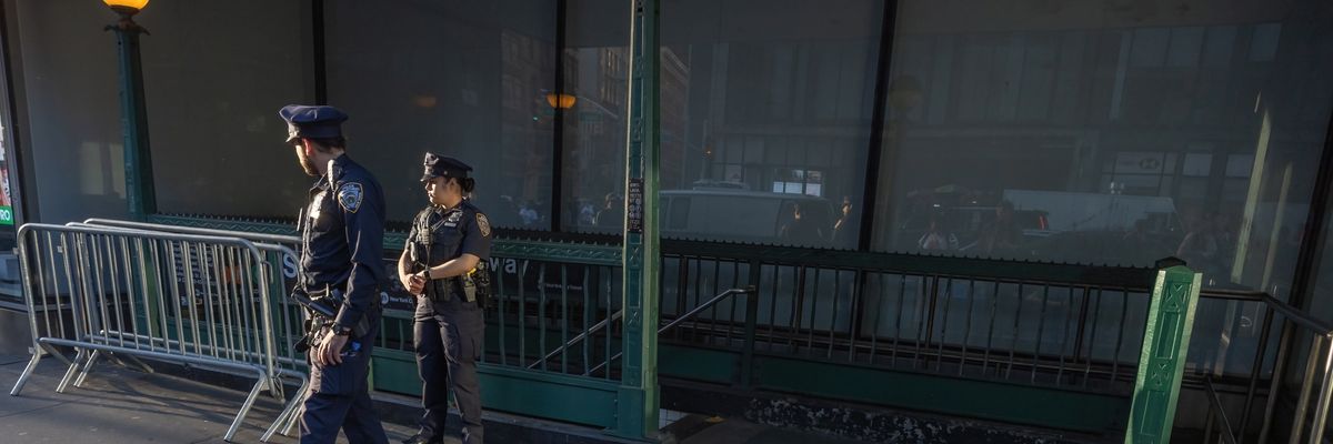 two police officers stand in front of a NYC subway entrance with #JORDANNEELY spray-painted on the ground