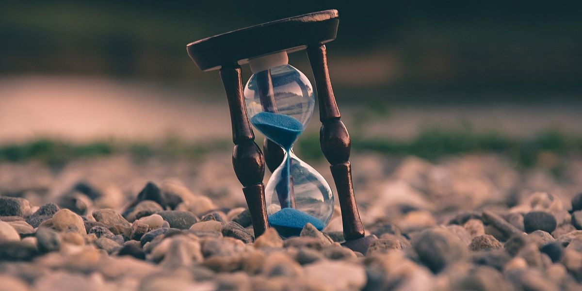 An hourglass with blue sand sits among a field of rocks