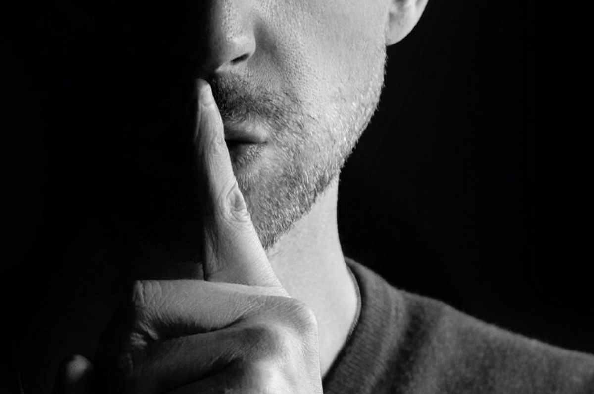 man holding finger to his mouth as a signal to be quiet