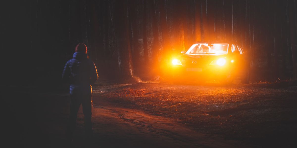 car headlights illuminating man in woods
