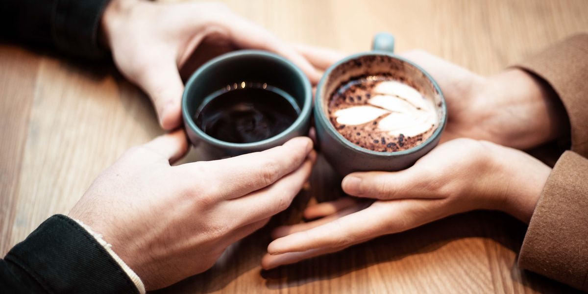 Closeup of two coffee-filled mugs held by a dating couple.