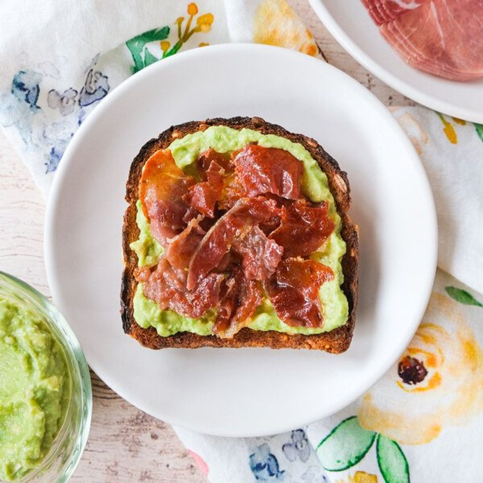 plate with toast smeared with avocado and topped with prosciutto