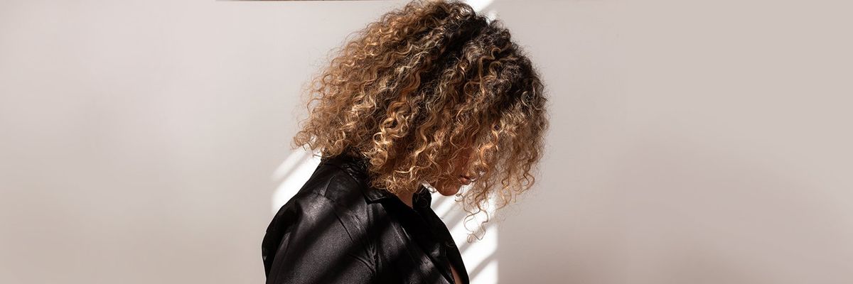 woman with curly hair standing with her head down in shame