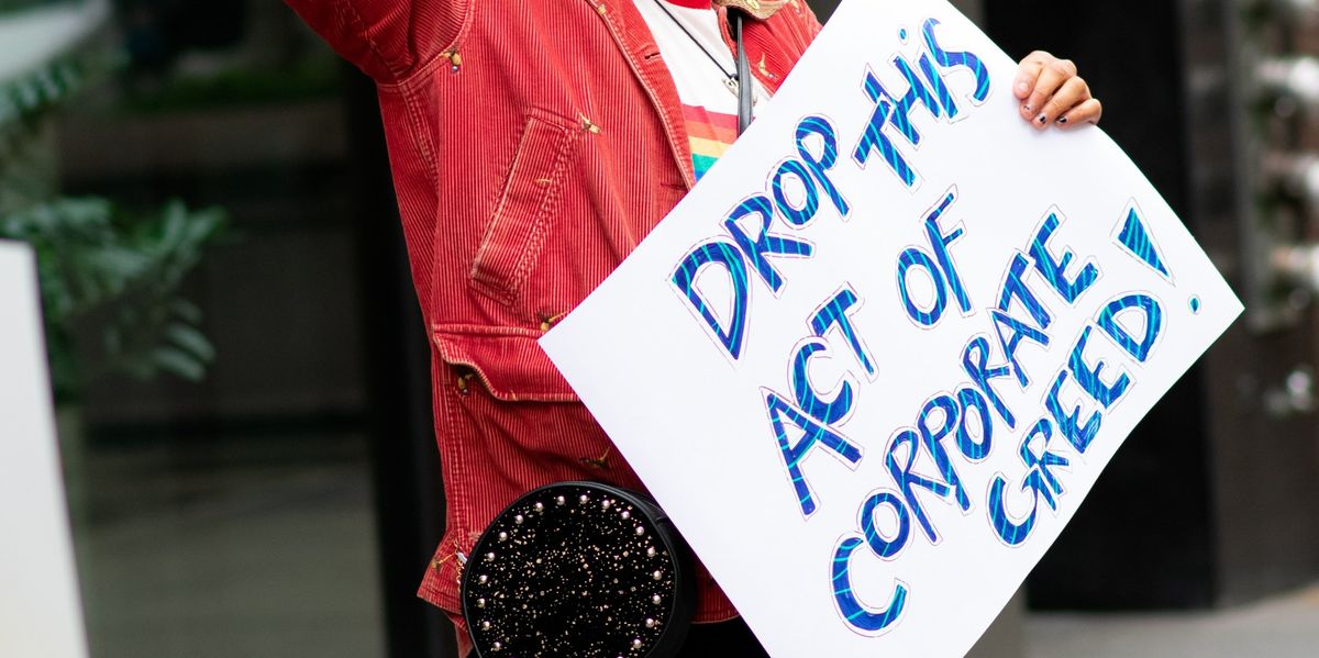 Demonstrator holds sign that reads, "Drop this act of corporate gree!"