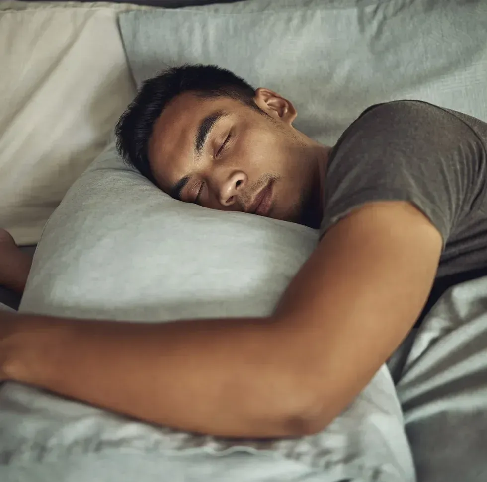 A man sleeps in bed hugging a grey pillow