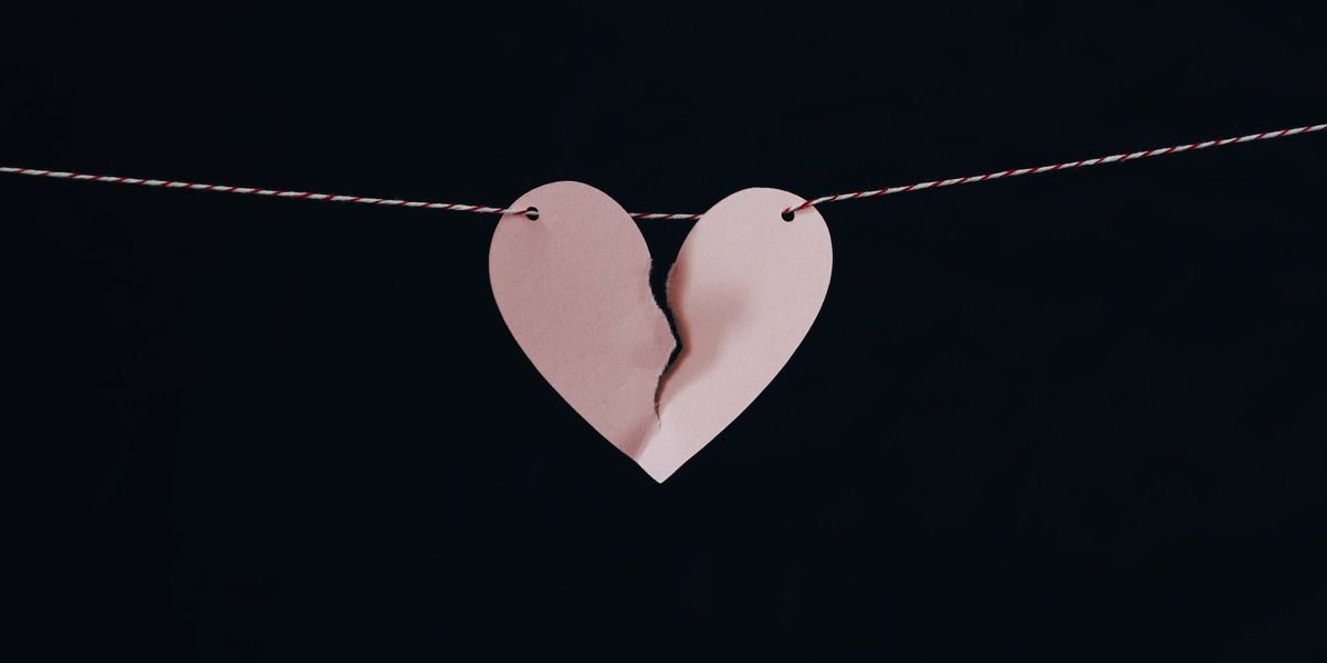 Picture of a pink heart tearing in two, hung off a red and white string, set against a black background