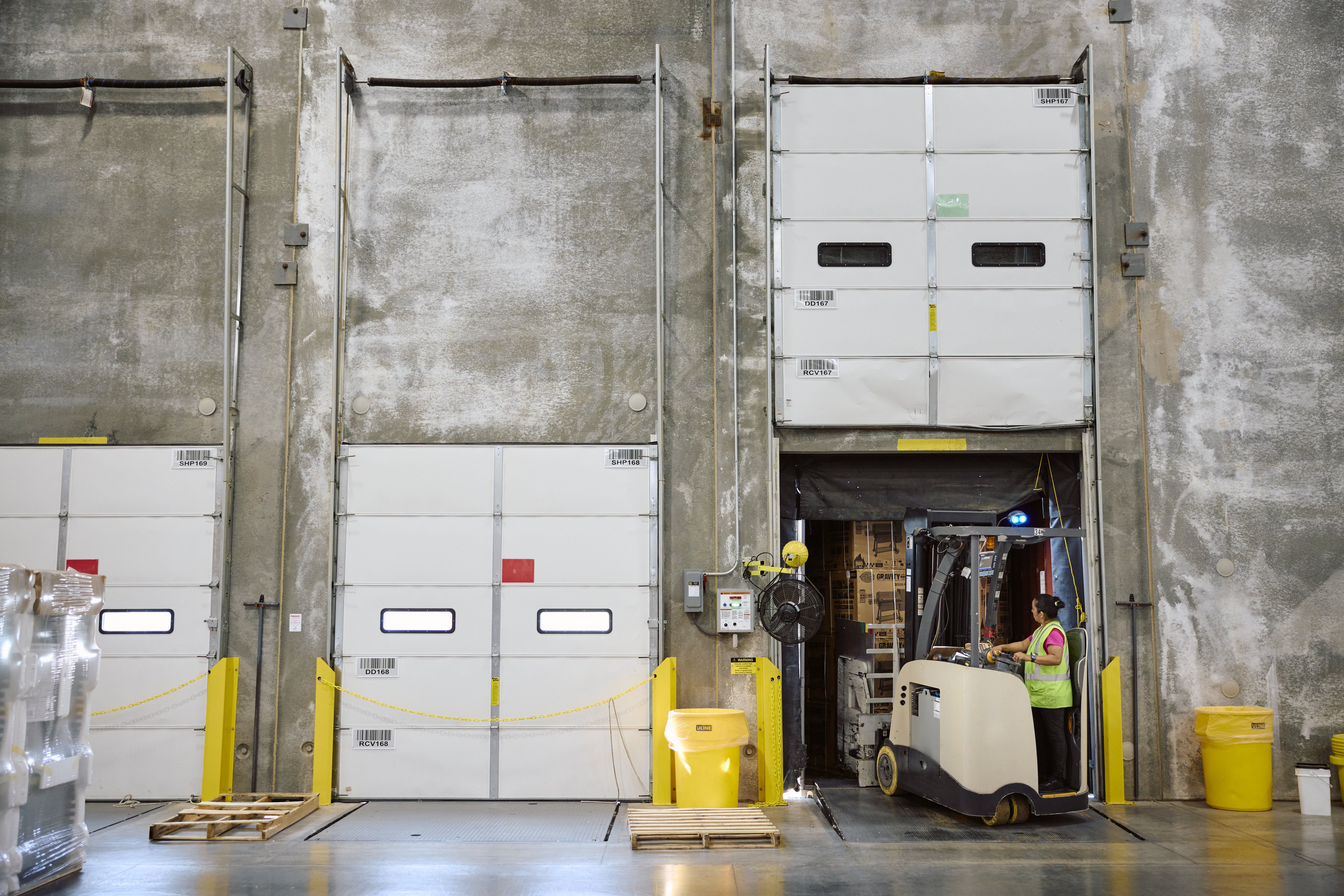 A retail warehouse worker uses a forklift to move boxes in a warehouse.