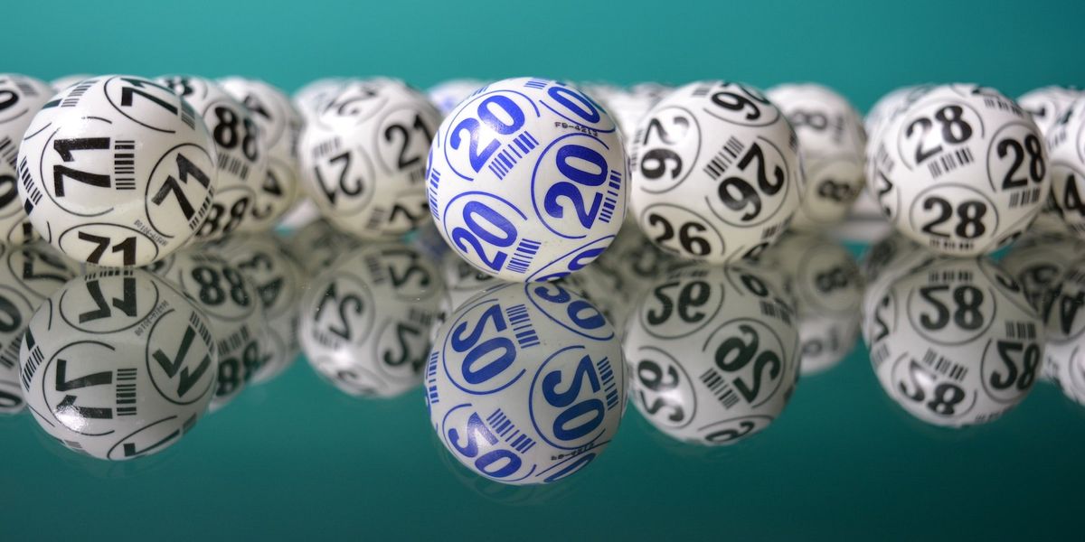 Several lotto balls lay on a mirrored floor; all the balls are white and black with different numbers except one that is white and blue, with the number 20