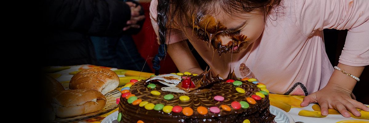 young girl has icing all over her face after having her face pushed into a chocolate birthday cake