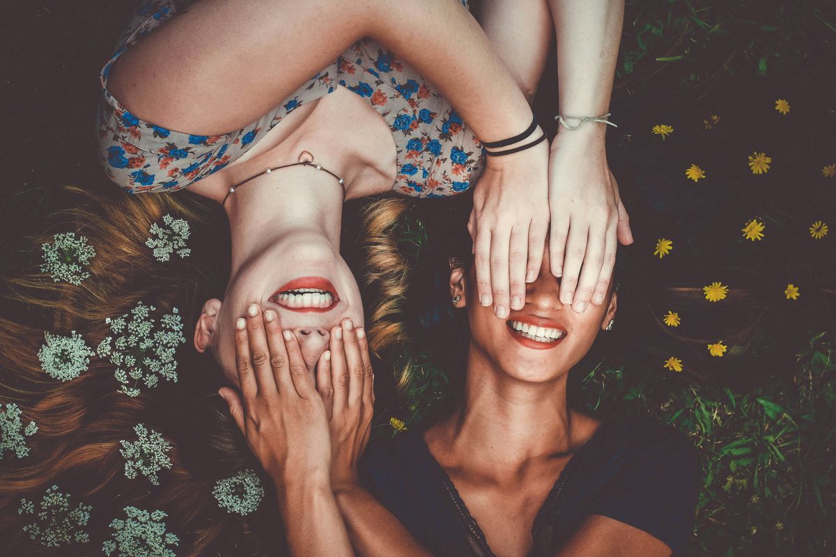 two women smiling with their hands over each other's eyes