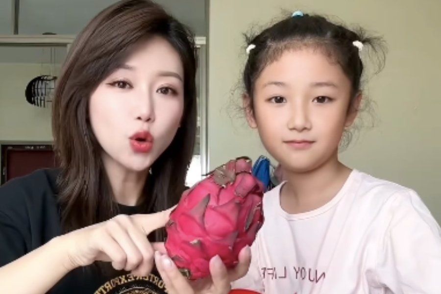 a girl standing next to her mom who is holding a dragon fruit