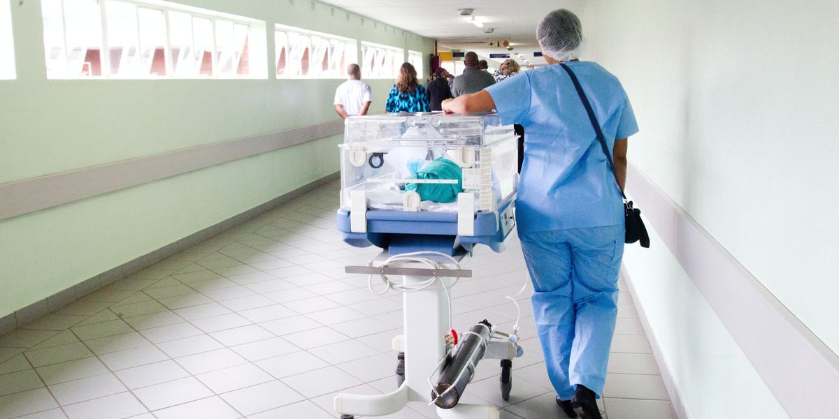 Orderly walking an incubator down a hospital corridor.