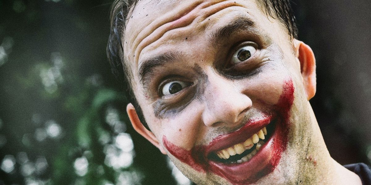 Close-up of a man wildly smiling with his face painted like the joker