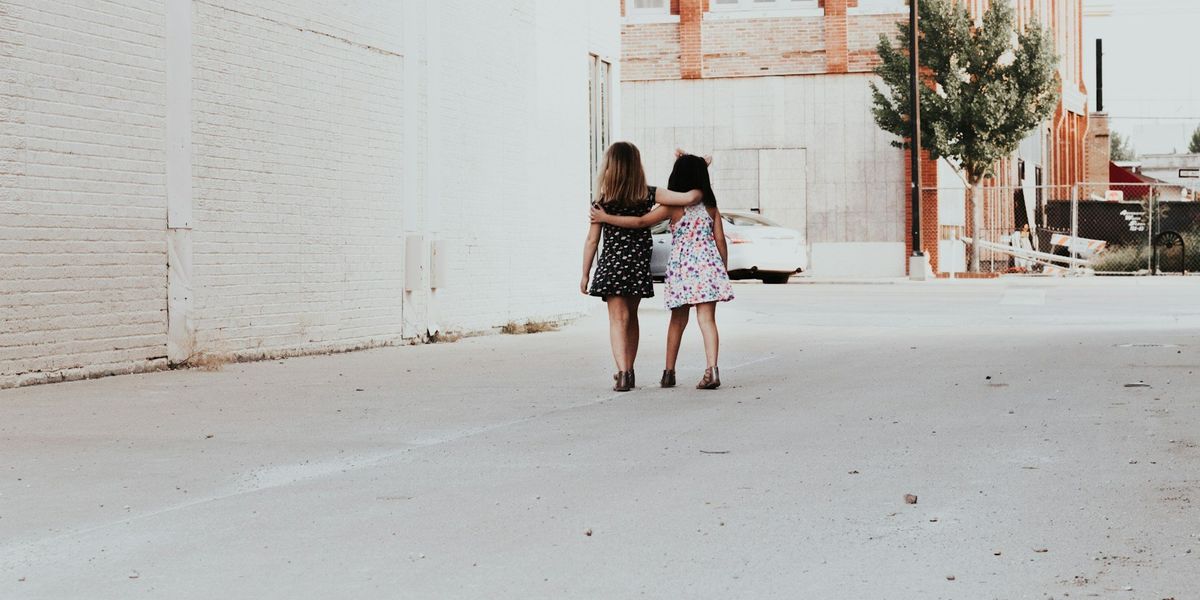 Two young girls walk away with their arms around one another