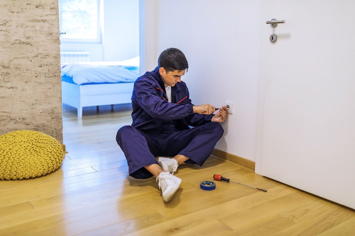 an electrician sitting on the floor installing a smart outlet in a home.