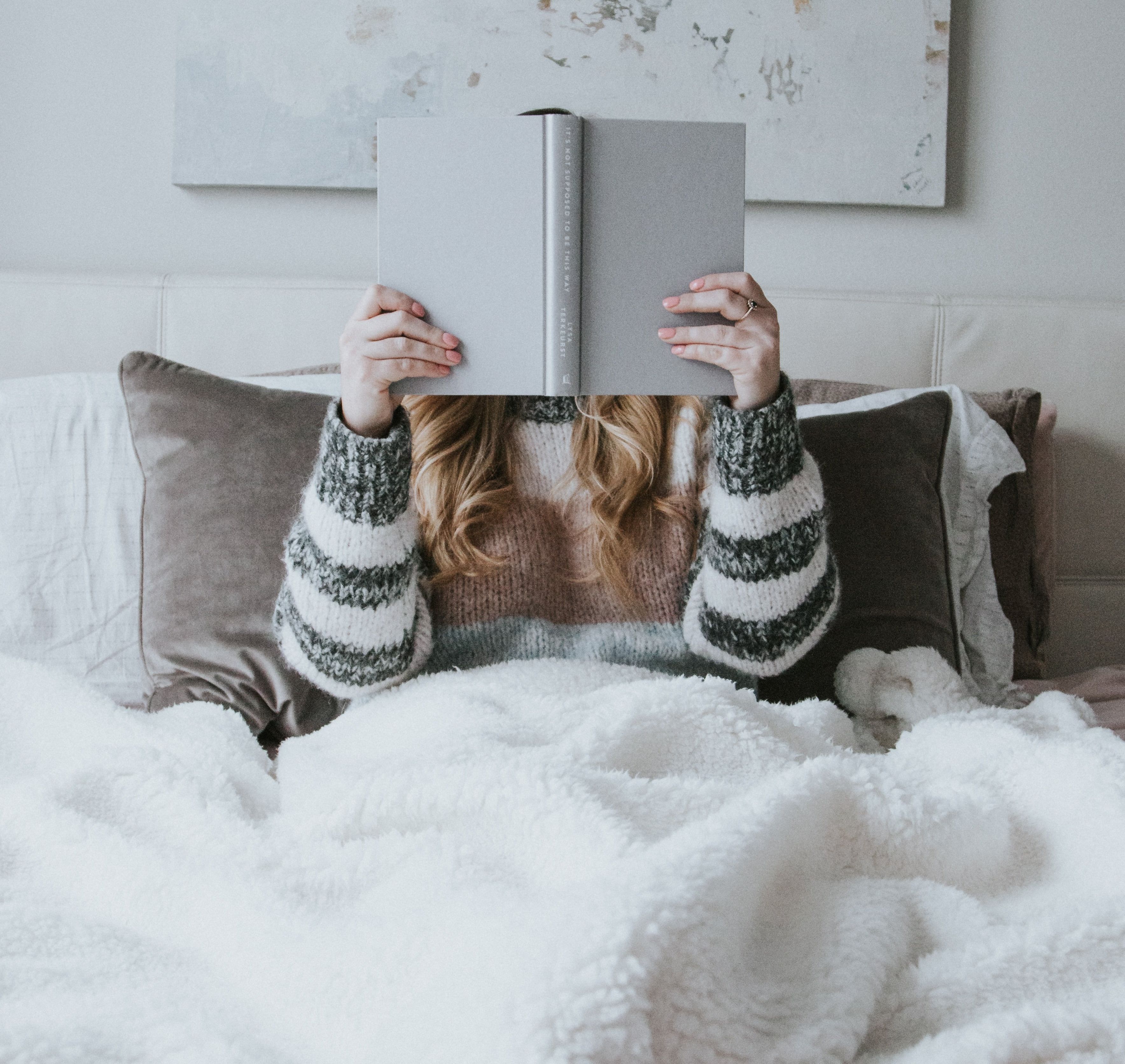 woman reading under a fluffy blanket