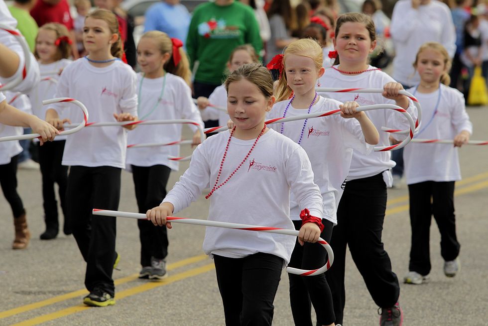 A group of dancers in matching outfits carrying candy canes march during a Christmas parade.