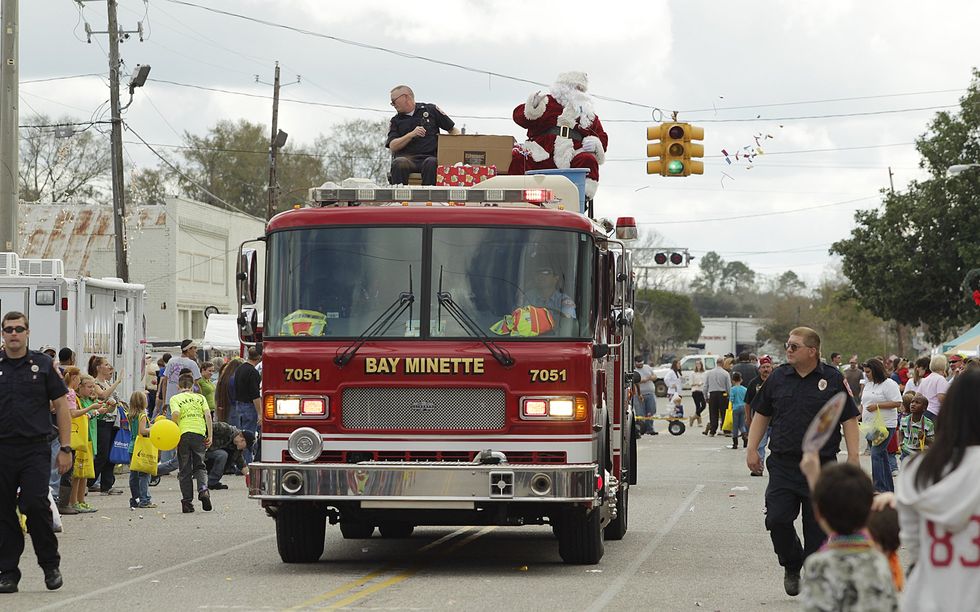 Santa waves to crowd while sitting on top of a red fire truck during a Christmas parade.