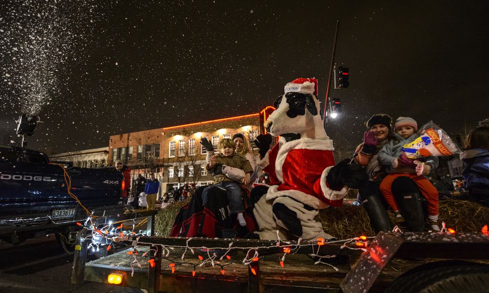 A snow machine pumps snow into the air as it falls over a float carrying people waving during a Christmas parade.