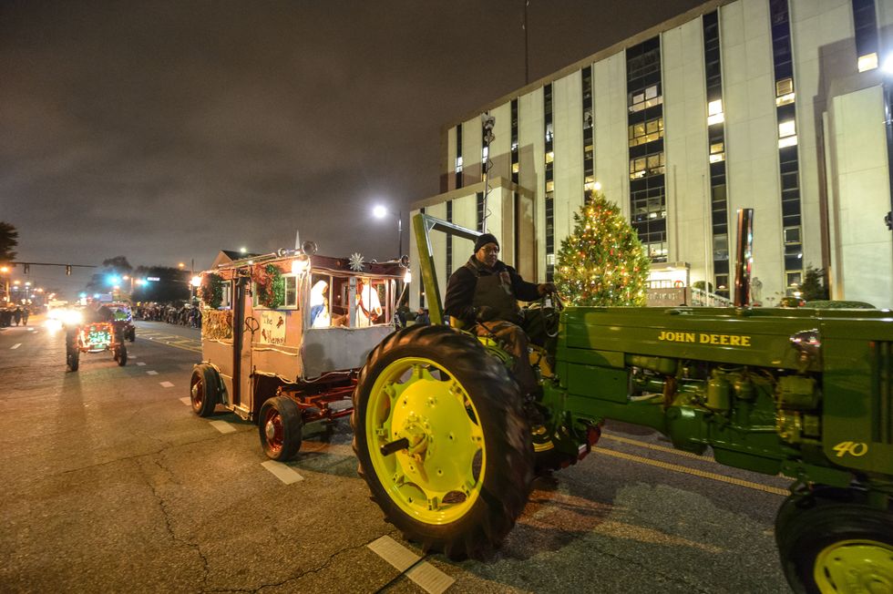 A green John Deere tractor pulls a decorated trailer with kids riding in it during a Christmas parade.