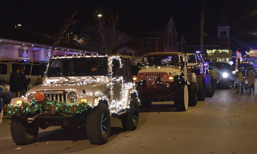 A line of jeeps, covered in decorations and twinkle lights, makes it way down the street in a Christmas parade.