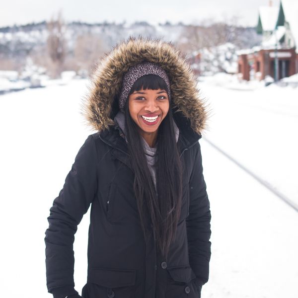 Black-woman-wearing-coat-standing-on-snow-and-smiling-during-daytime