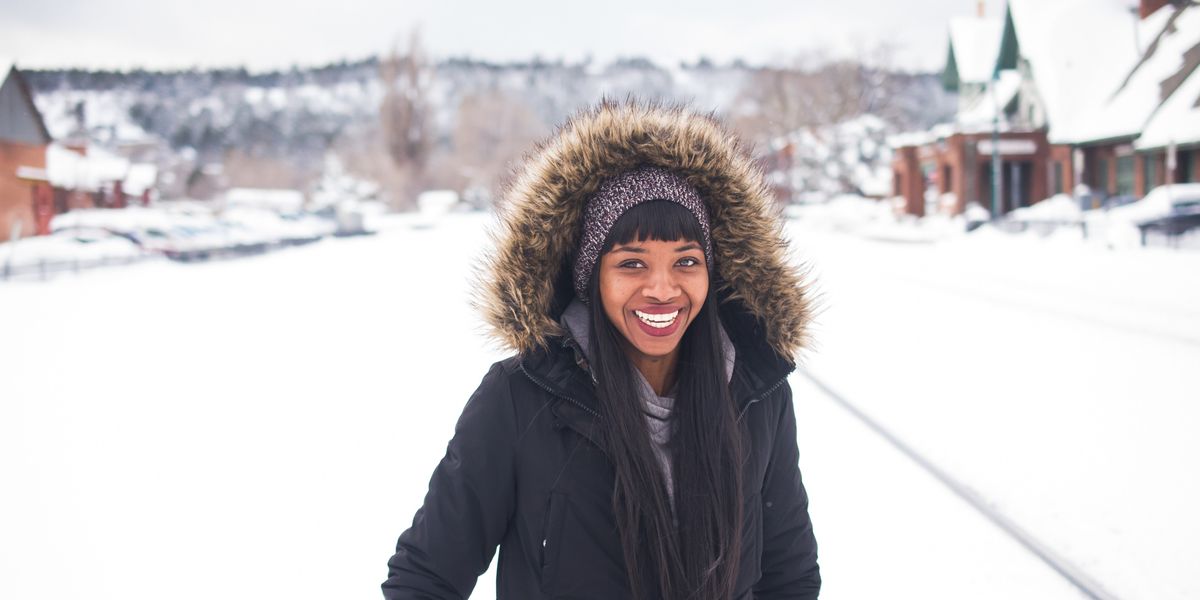 Black-woman-wearing-coat-standing-on-snow-and-smiling-during-daytime