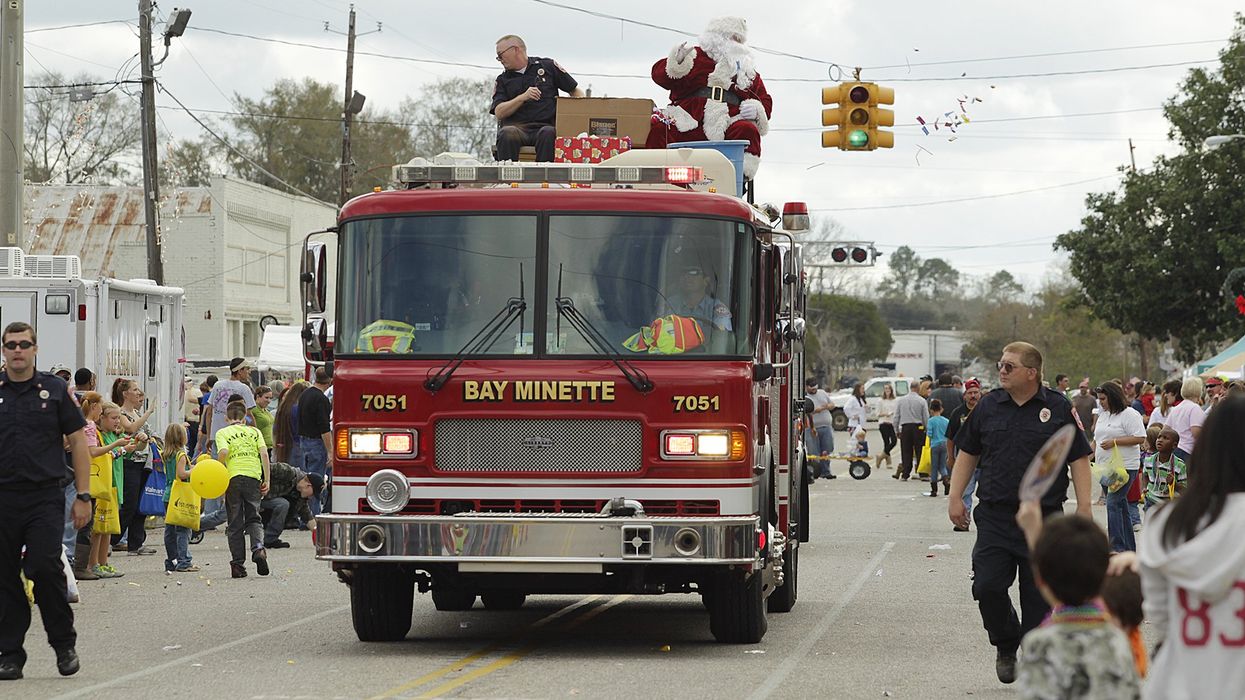 Santa waves to crowd while sitting on top of a red fire truck during a Christmas parade.