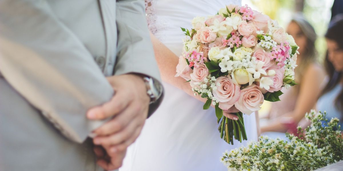 Close up, mid-section shot of a bride and groom at the altar, his hands clasped, her's holding her bouquet