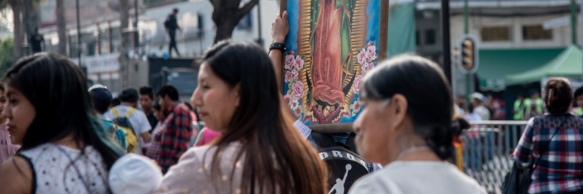women walk in a crowd with the virgin of guadalupe in a painting behind them 