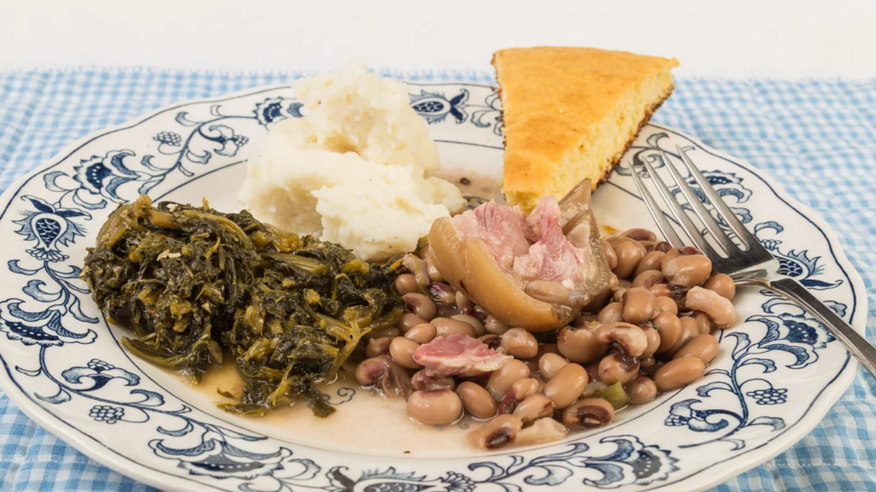 White and blue plate with collard greens, black-eyed peas, ham, mashed potatoes and cornbread.