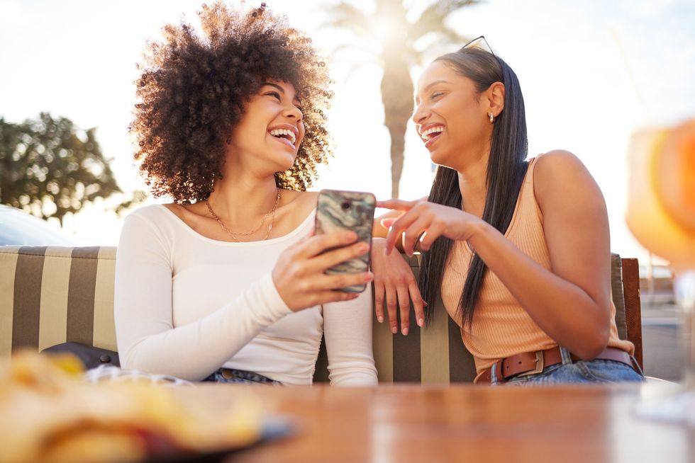 two-women-at-a-restaurant-laughing-together-over-something-funny-on-their-phone